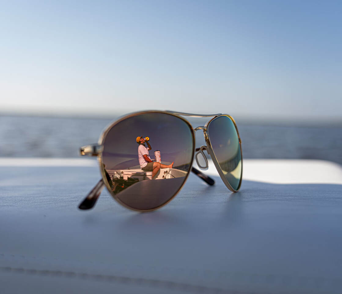 Aviator sunglasses on a beach with a fishing reflection